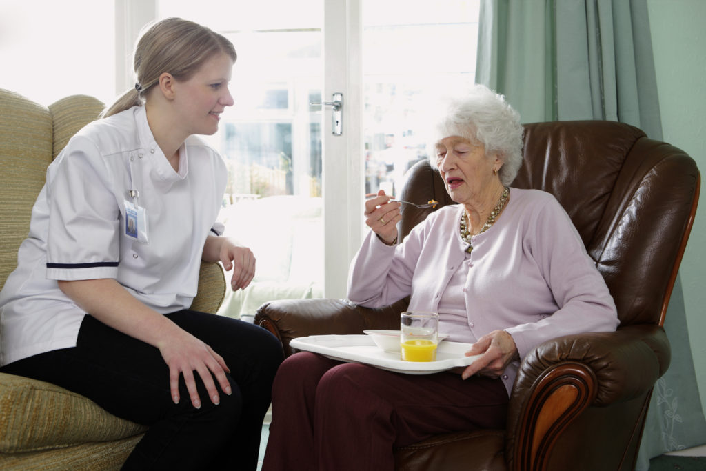 carer helps her elderly pactient by making sure she eats her a meal